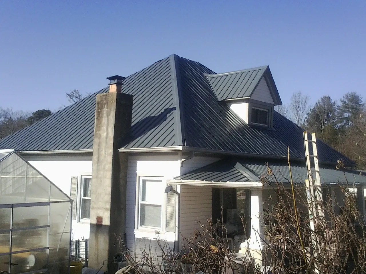 Dark blue standing seam metal roof on a white farmhouse with dormer — Slate & Tile Roof Repair by Roofing Brothers in Gadsden
