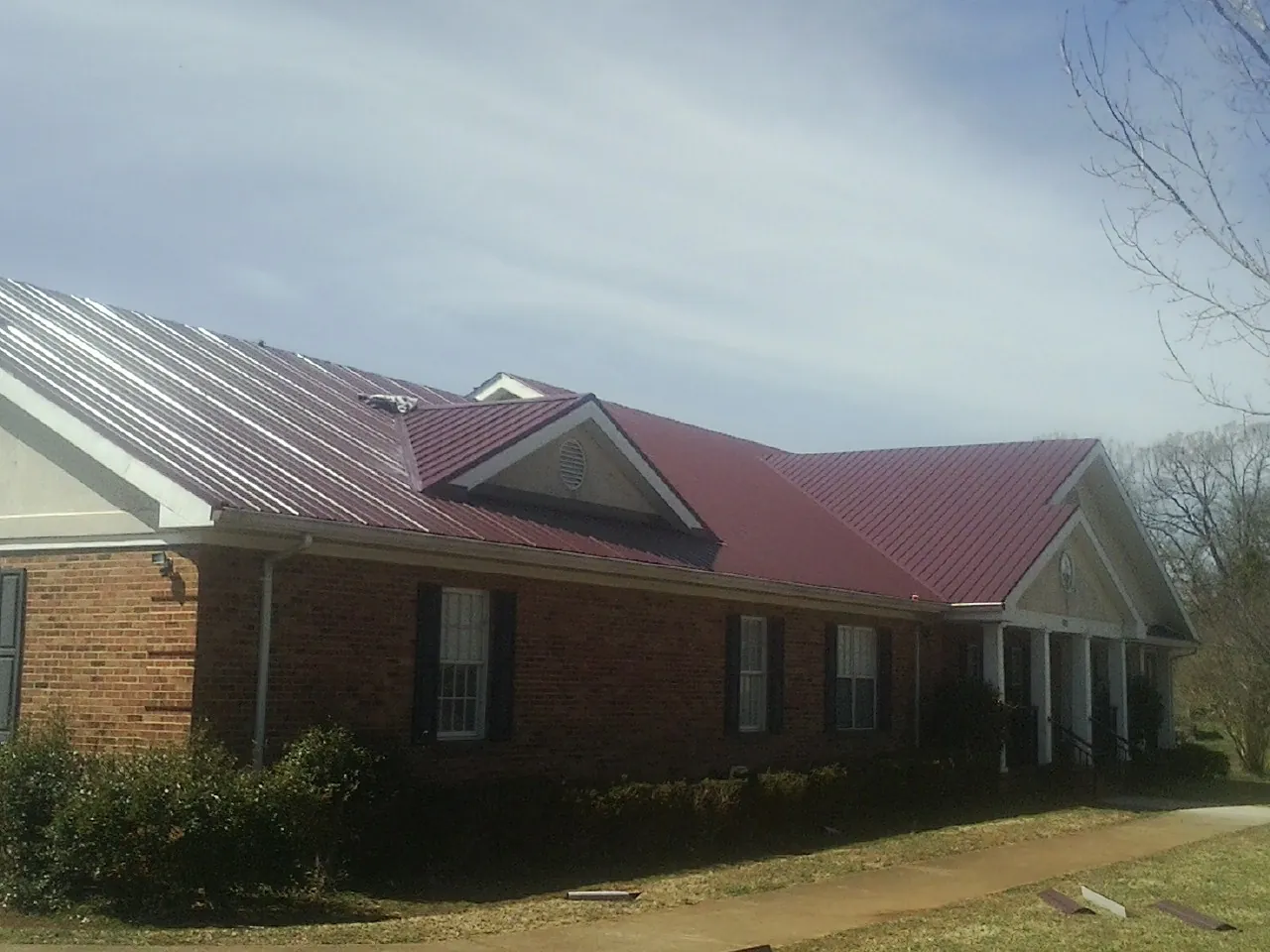 Red metal roof with gabled entries on a long brick building, from a Hail Damage Roof Repair job in Gadsden