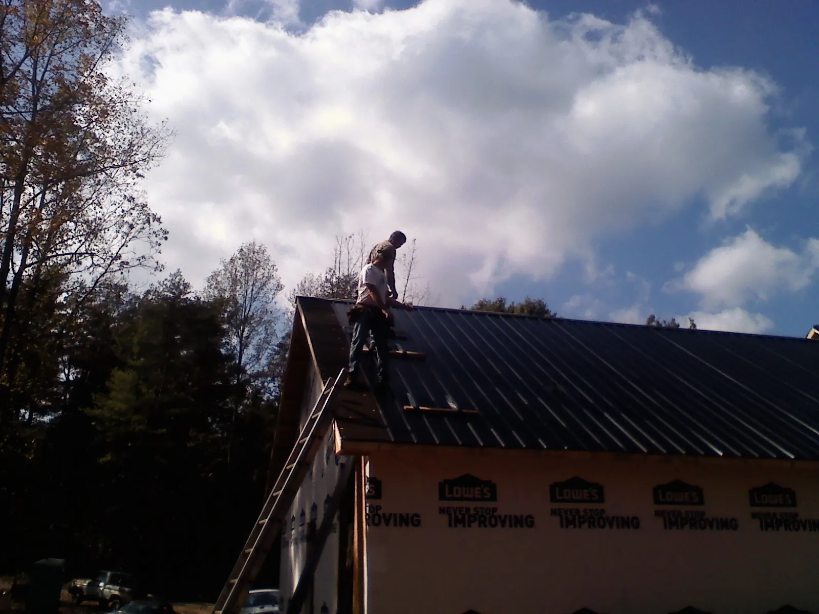 Roofer fastening dark metal panels high against a cloudy sky, from a Roof Inspection job in Gadsden